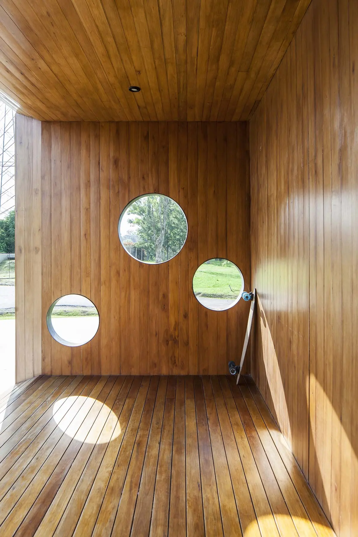 Espaço externo com revestimento de madeira e janelas circulares — projeto Santa Isabel, por Arfuso Arquitectos, em Ingeniero Maschwitz