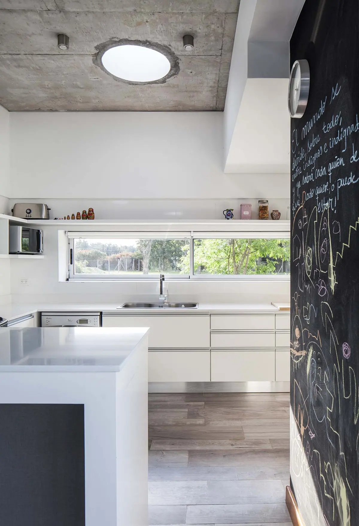 Cocina moderna con isla blanca, techo de hormigón y pared de pizarra — proyecto Santa Isabel, por Arfuso Arquitectos, en Ingeniero Maschwitz