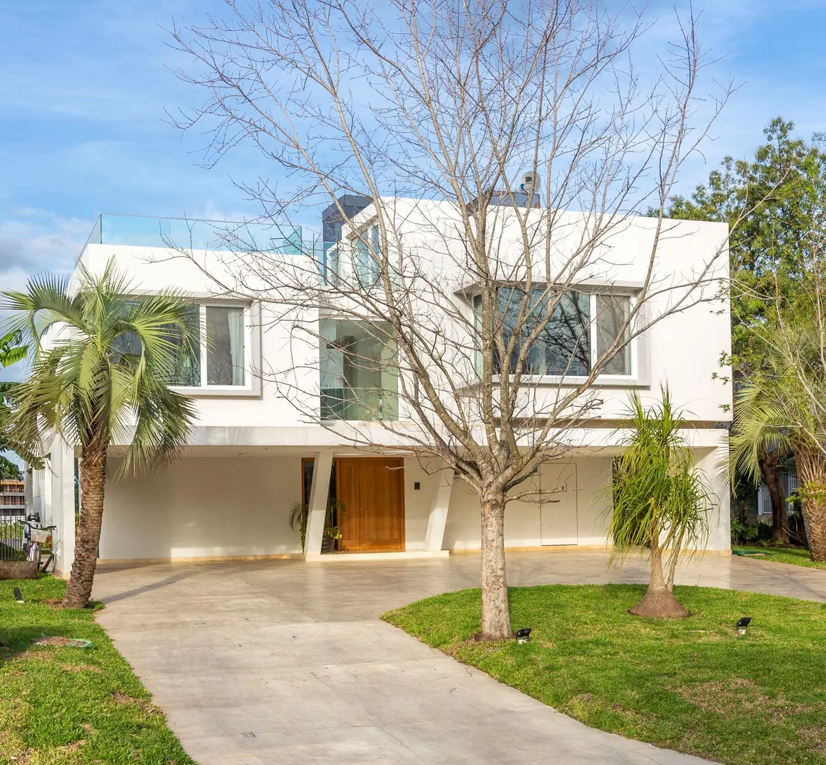 Fachada de casa moderna branca de concreto com janelas do chão ao teto e árvores nuas — projeto Las Caletas, por Arfuso Arquitectos, em Nordelta