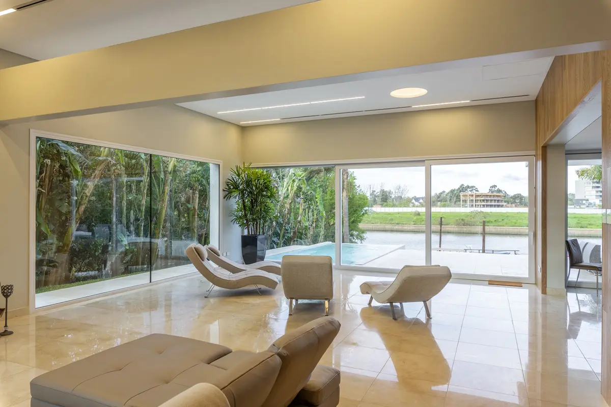 Living moderno con ventanales amplios y vista a piscina — proyecto Las Caletas, por Arfuso Arquitectos, en Nordelta