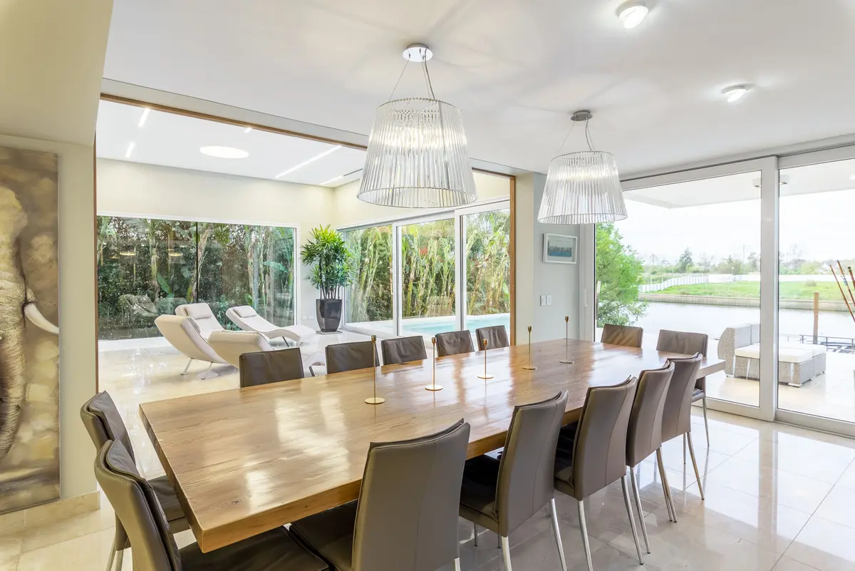 Sala de jantar moderna com mesa longa de madeira e lustres grandes — projeto Las Caletas, por Arfuso Arquitectos, em Nordelta