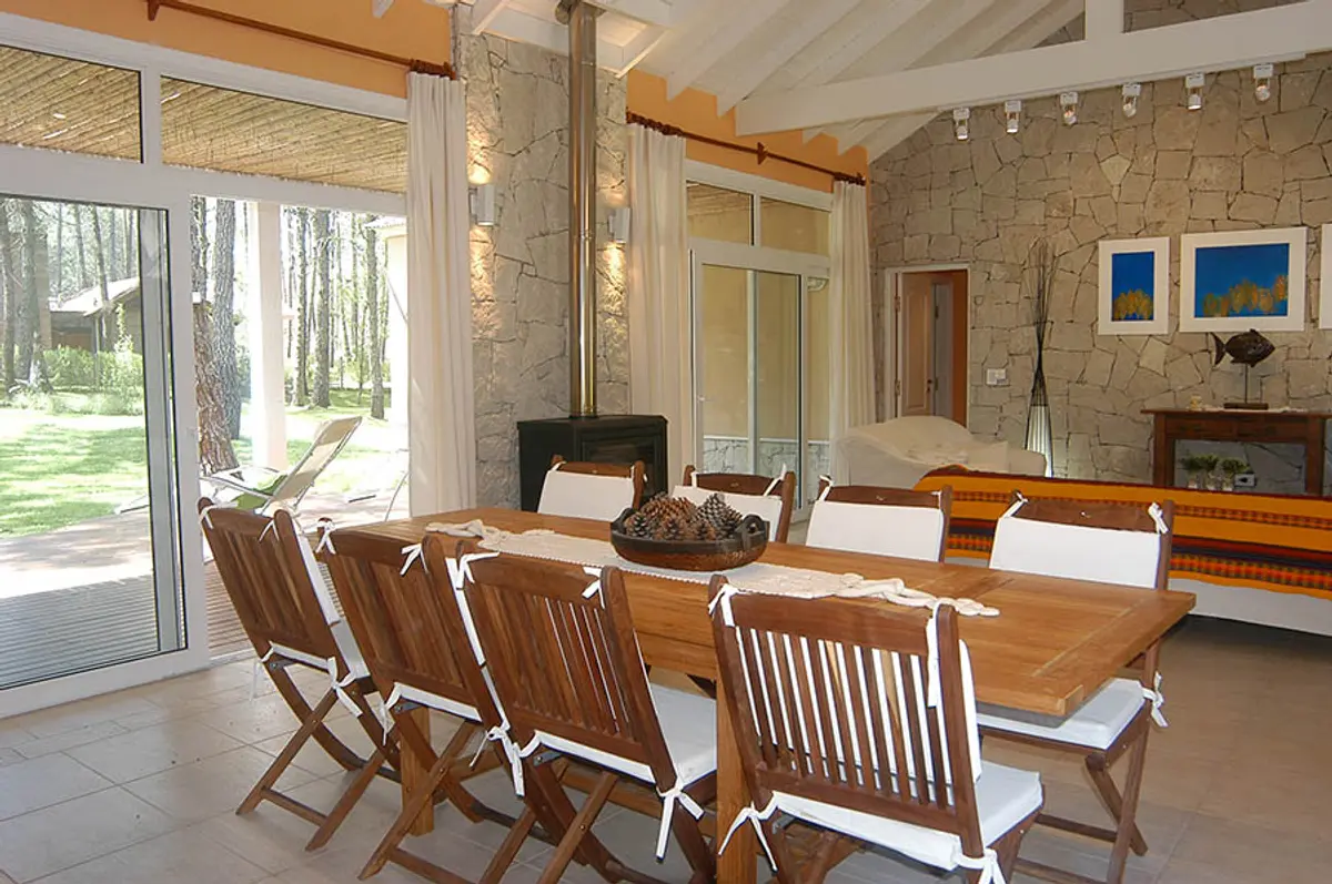 Sala de jantar rústica com parede de pedra e vigas de madeira — projeto Casa Cariló 2005, por Hugo Zawadski Arquitectos, em Cariló