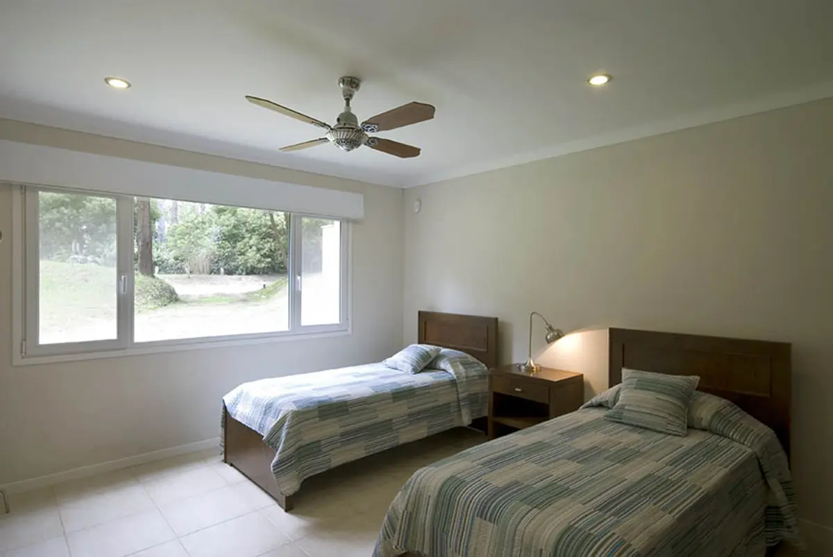 quarto moderno com duas camas, luz natural e ventilador de teto — projeto Casa Cariló 2007, por Hugo Zawadski Arquitectos, em Cariló