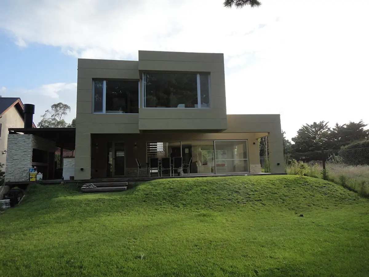 casa moderna com janelas amplas e gramado em declive — projeto Casa Valeria del Mar 2015, por Hugo Zawadski Arquitectos, em Valeria del Mar