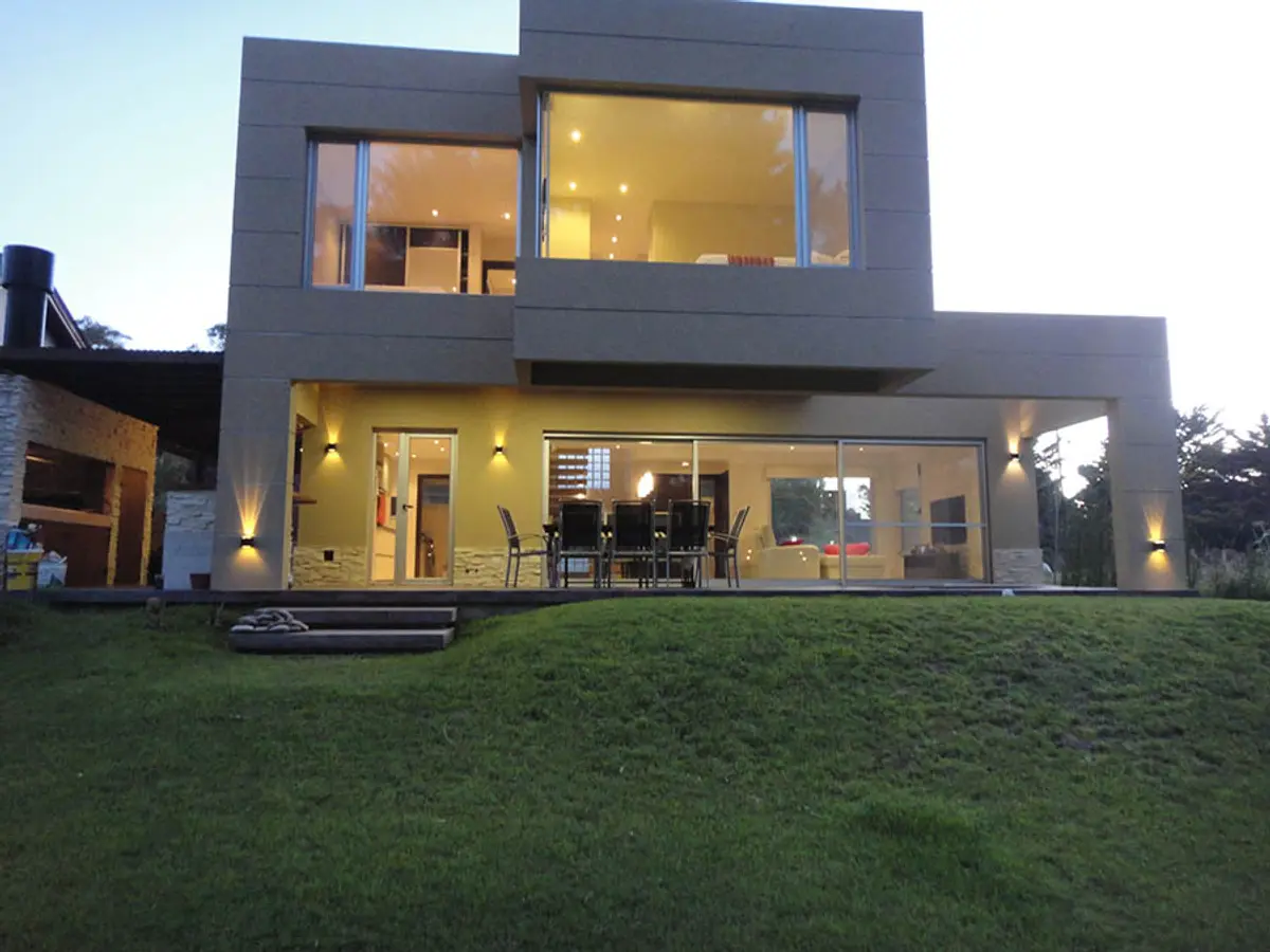 fachada moderna con amplios ventanales y césped — proyecto Casa Valeria del Mar 2015, por Hugo Zawadski Arquitectos, en Valeria del Mar