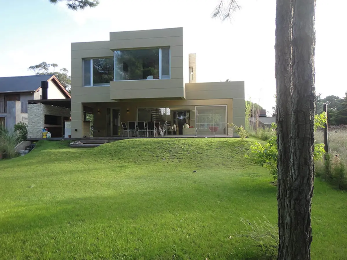 fachada moderna com grandes janelas e pergolado em bairro suburbano — projeto Casa Valeria del Mar 2015, por Hugo Zawadski Arquitectos, em Valeria del Mar