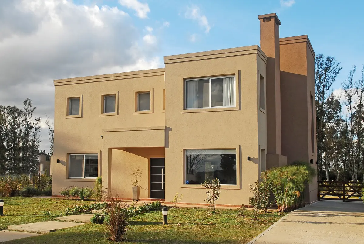 Casa moderna de dois andares com fachada bege e detalhes em bordô — projeto Casa El Recodo, por Fhee Construcciones, em Garin