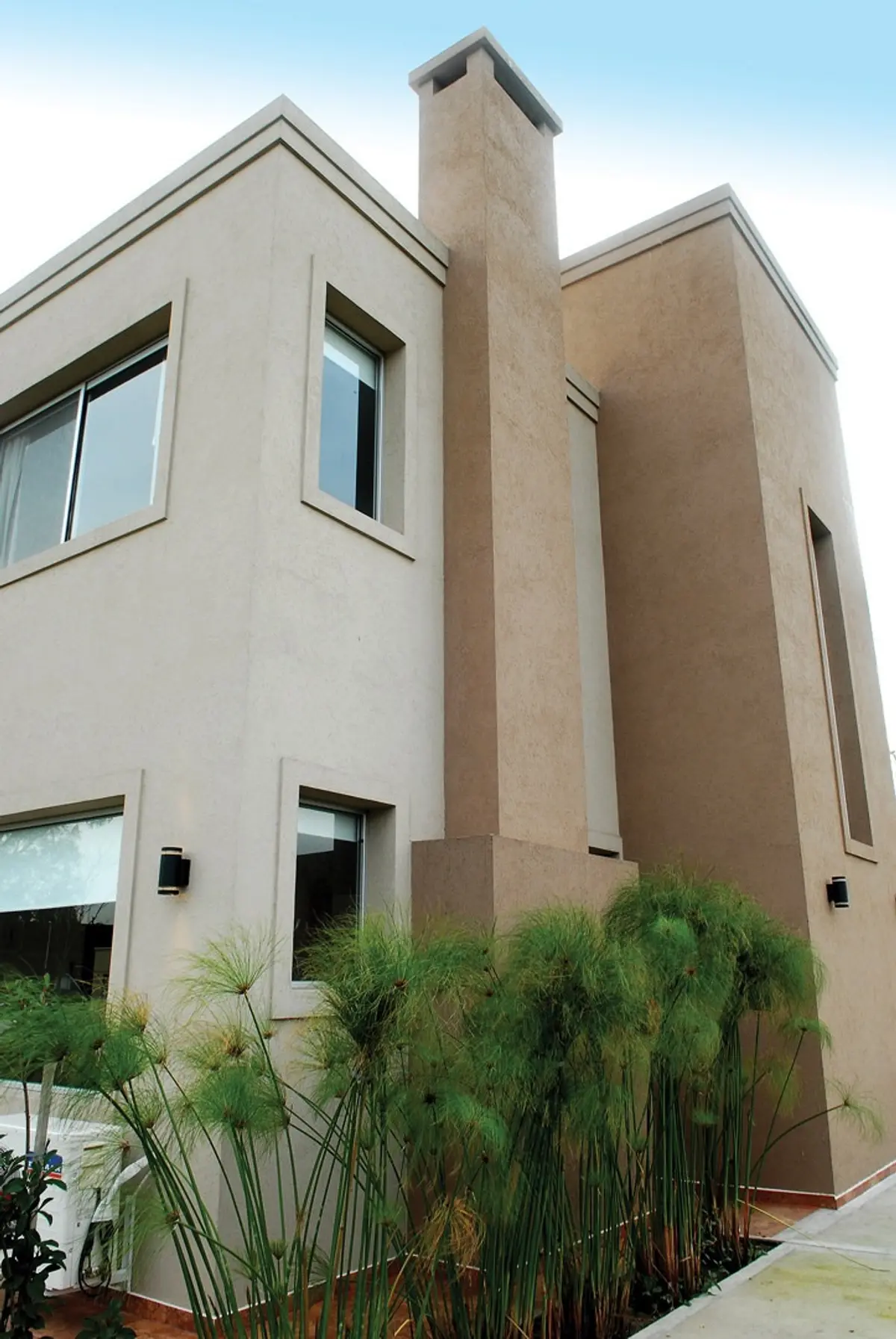 Fachada moderna com vegetação exuberante e chaminé alta — projeto Casa El Recodo, por Fhee Construcciones, em Garin