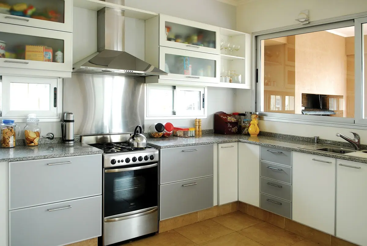 Cocina moderna con electrodomésticos de acero inoxidable y muebles blancos — proyecto Casa El Recodo, por Fhee Construcciones, en Garin
