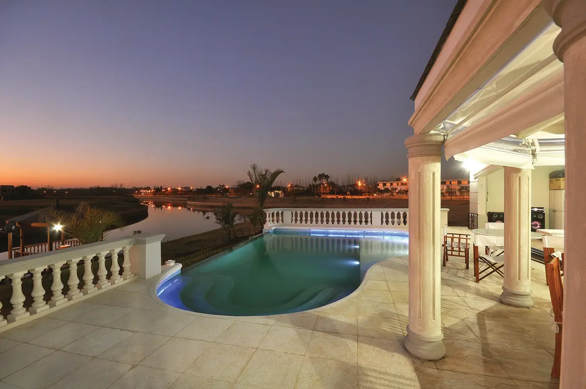 Área de piscina de estilo mediterráneo moderno al atardecer con luces cálidas — proyecto Casa 4, por Fhee Construcciones, en Nordelta