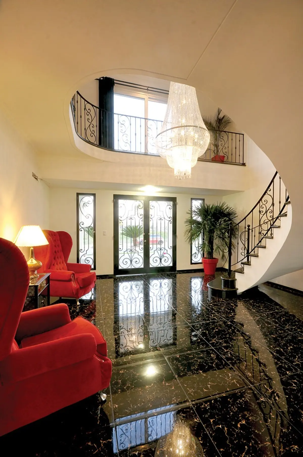 Hall de entrada palaciano com escada em caracol, lustre de cristal e poltronas vermelhas — projeto Casa 4, por Fhee Construcciones, em Nordelta