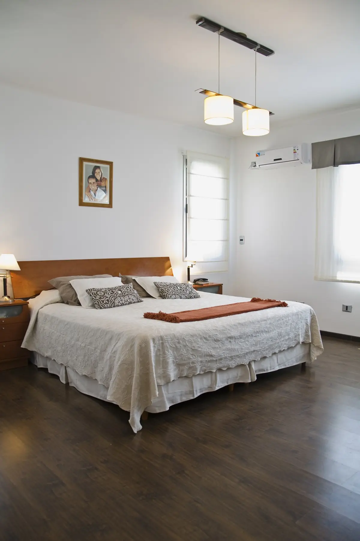 Quarto moderno com cama de casal, piso de madeira escura e luminária pendente linear — projeto Casa 3, por Fhee Construcciones, em Rincón de La Costa