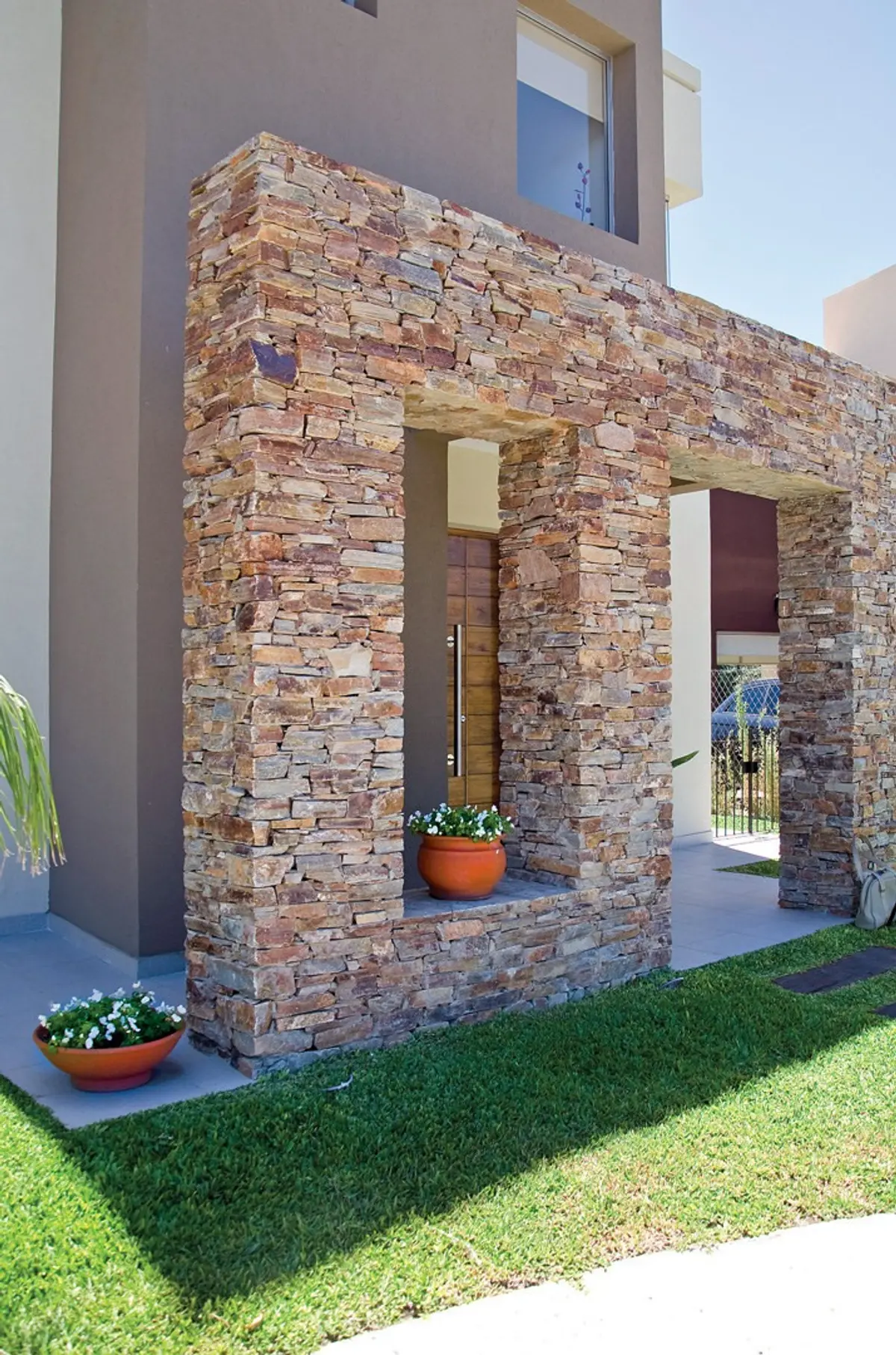 Fachada moderna con piedra apilada, entrada arqueada y macetas — proyecto Casa 3, por Fhee Construcciones, en Rincón de La Costa