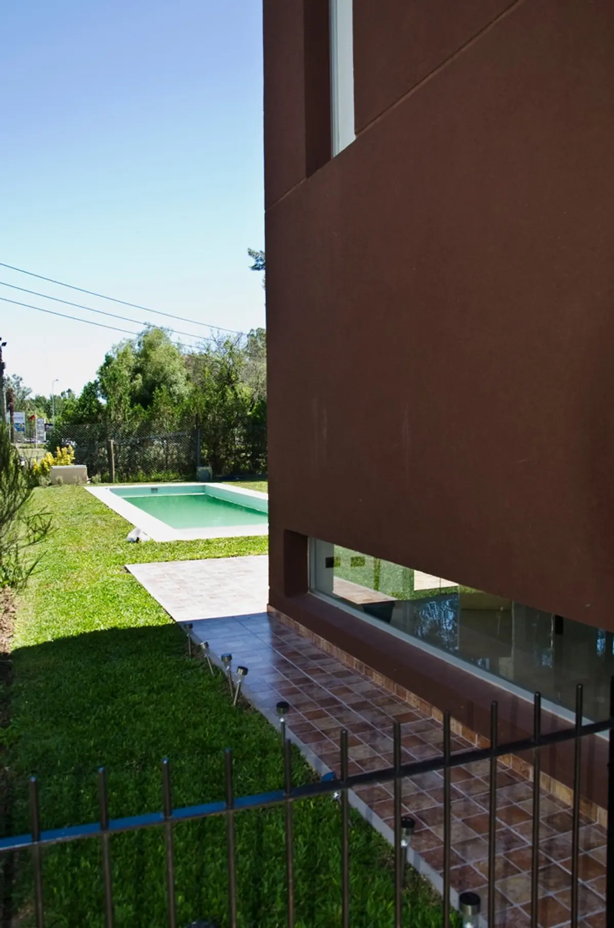 Piscina moderna com gramado e fachada marrom-avermelhada — projeto Casa 2, por Fhee Construcciones, em Rincón de La Costa