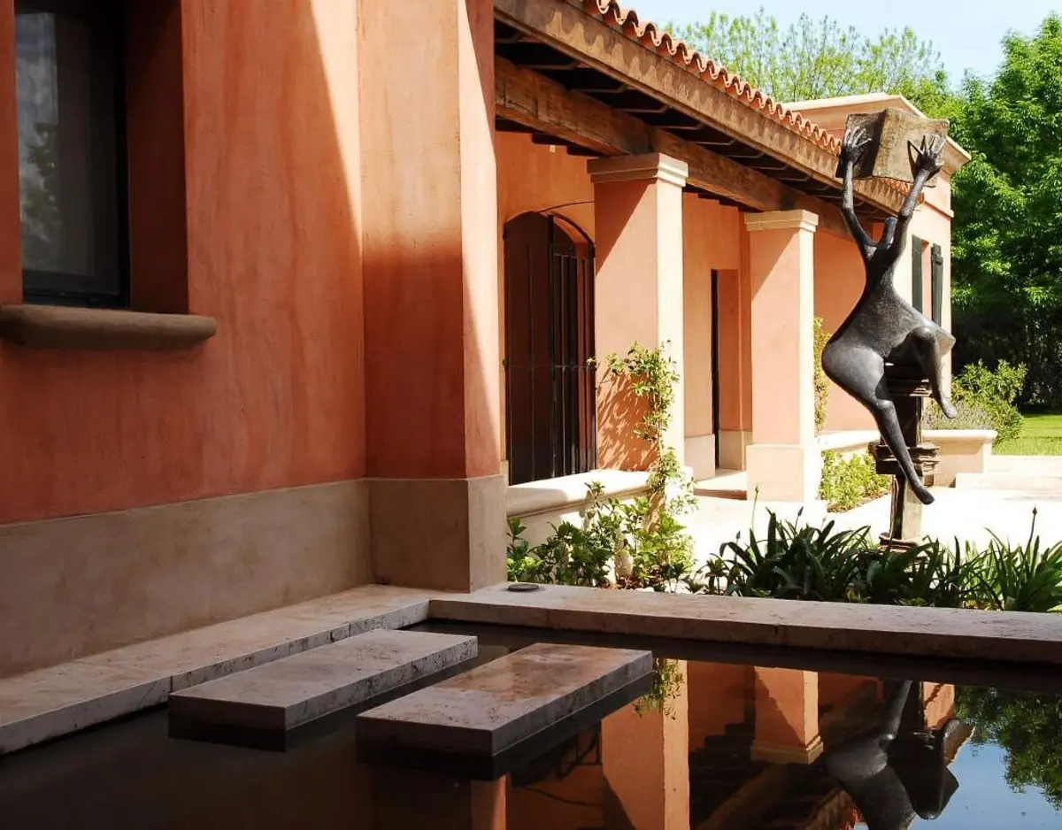 fachada mediterránea con escultura de bronce y estanque — proyecto Aire de Campo, por Ricardo Pereyra Iraola 