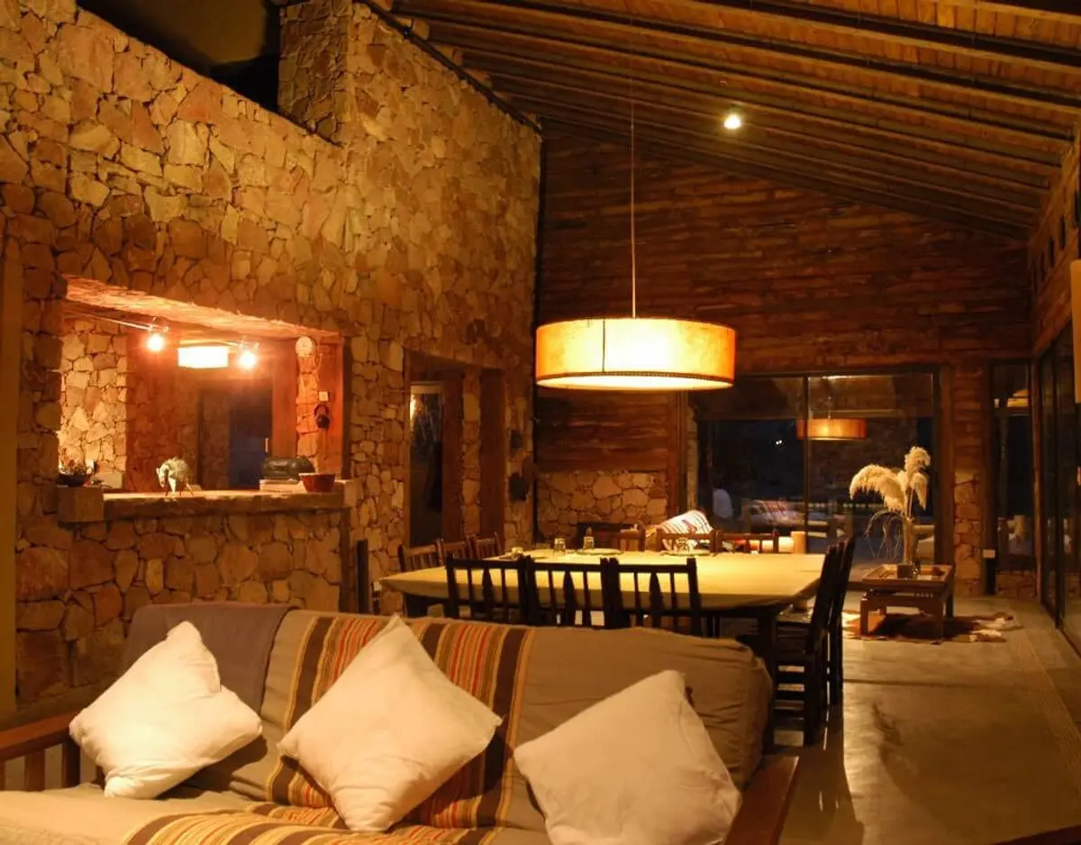 Living comedor rústico con paredes de piedra y vigas de madera — proyecto Cerro de Uspallata, por Ricardo Pereyra Iraola , en Uspallata