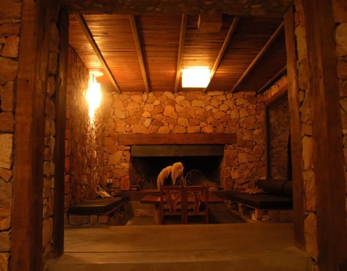 Sala rústica con paredes de piedra y vigas de madera — proyecto Cerro de Uspallata, por Ricardo Pereyra Iraola , en Uspallata
