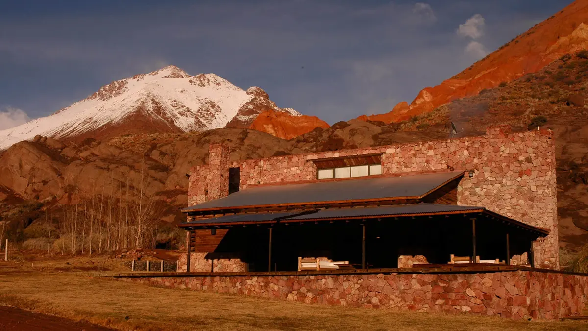 edificio rústico con pérgola ante montañas nevadas — proyecto Cerro de Uspallata, por Ricardo Pereyra Iraola , en Uspallata
