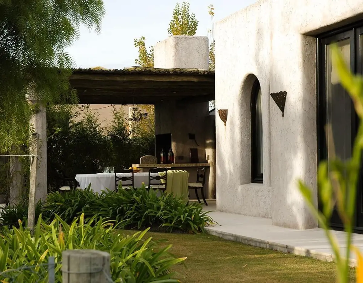 Fachada rústica mediterrânea com arcos e vegetação exuberante — projeto La Intriga, por Ricardo Pereyra Iraola