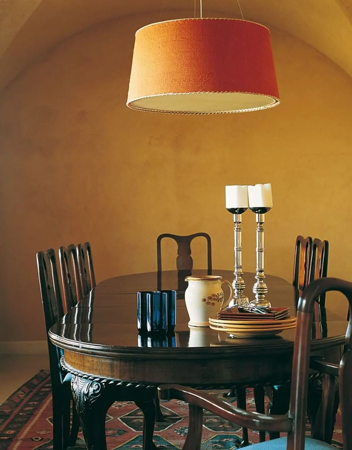 Comedor clásico con mesa redonda de madera oscura y lámpara colgante naranja — proyecto Las Arcadas, por Ricardo Pereyra Iraola 
