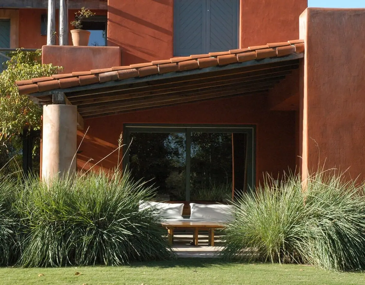 Fachada residencial mediterrânea com pérgola de madeira e vegetação exuberante — projeto Paisajismo Aire, por Ricardo Pereyra Iraola