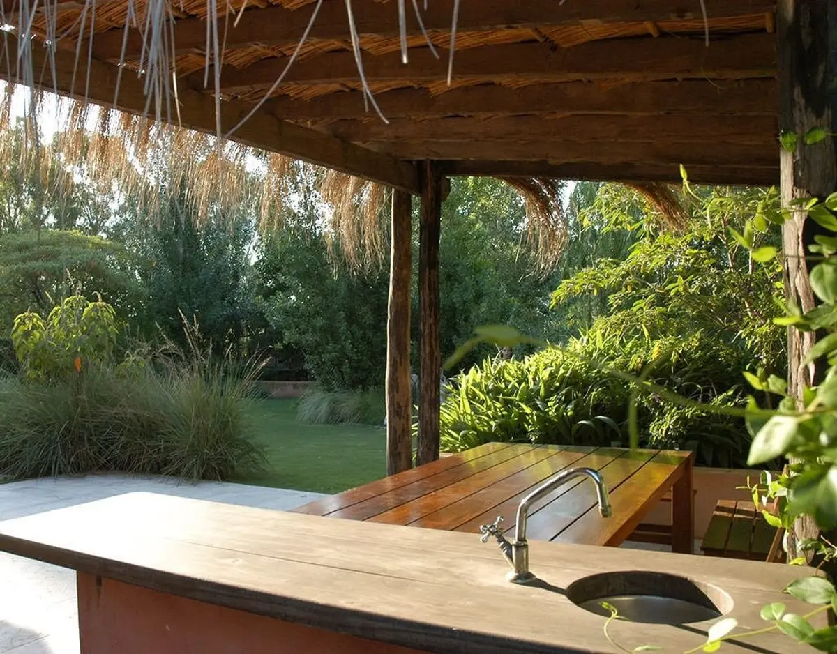 Pátio rústico com madeira, pérgola e vegetação exuberante — projeto Paisajismo Aire, por Ricardo Pereyra Iraola