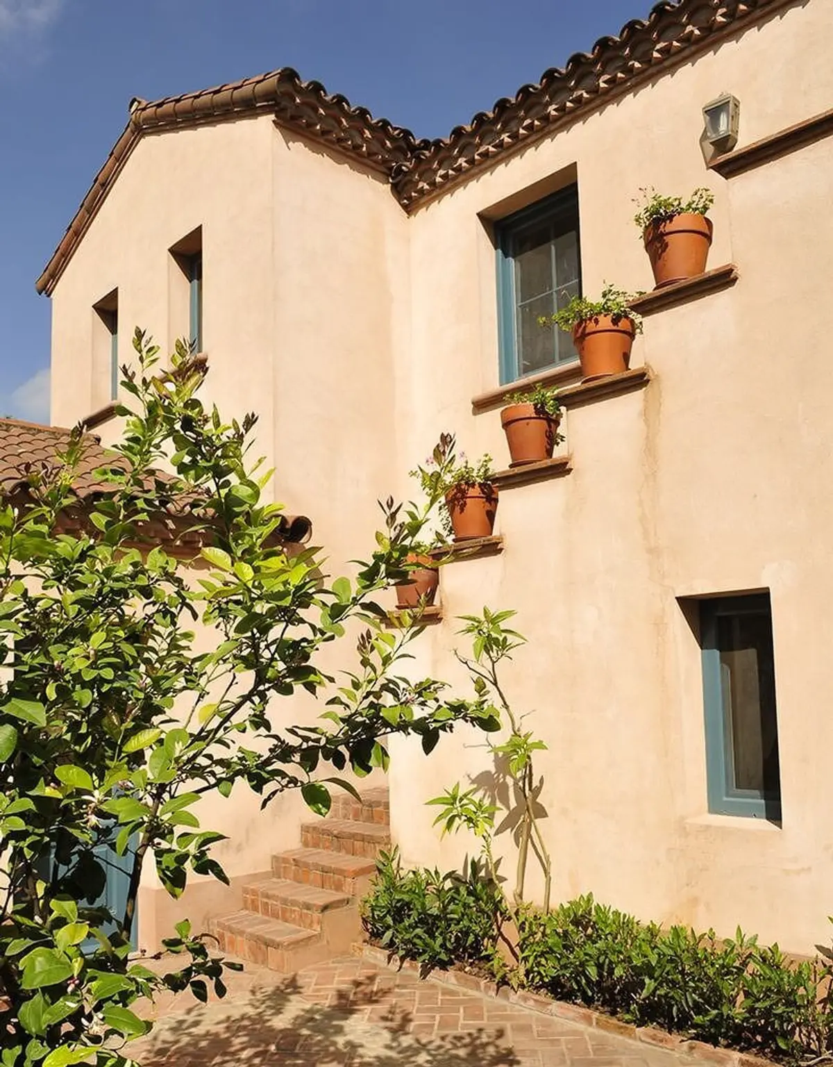 Fachada mediterrânea com vasos de terracota e escada de tijolos — projeto Un Patio Adelante, por Ricardo Pereyra Iraola
