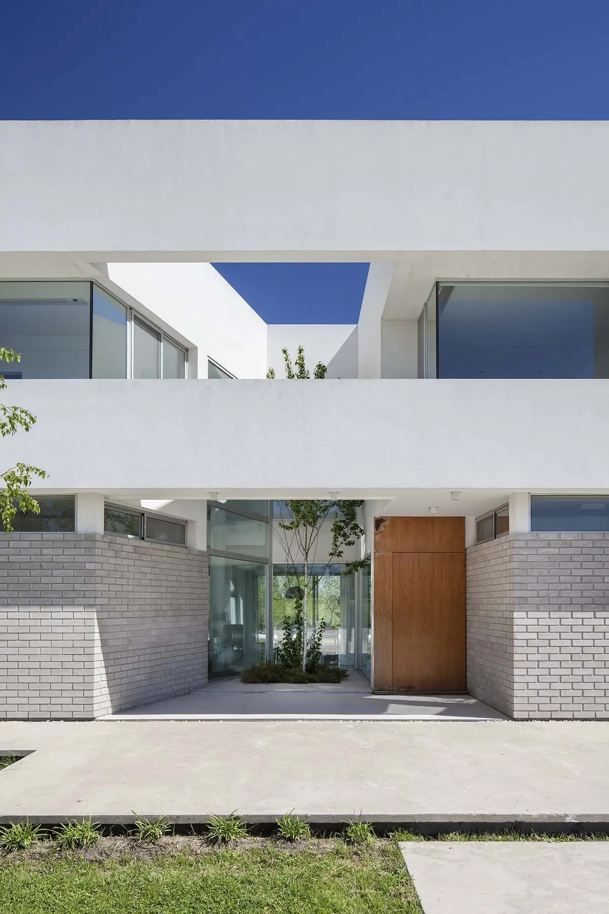 Fachada moderna blanca con entrada de madera y jardín interior — proyecto Casa MA, por Estudio GR, en City Bell