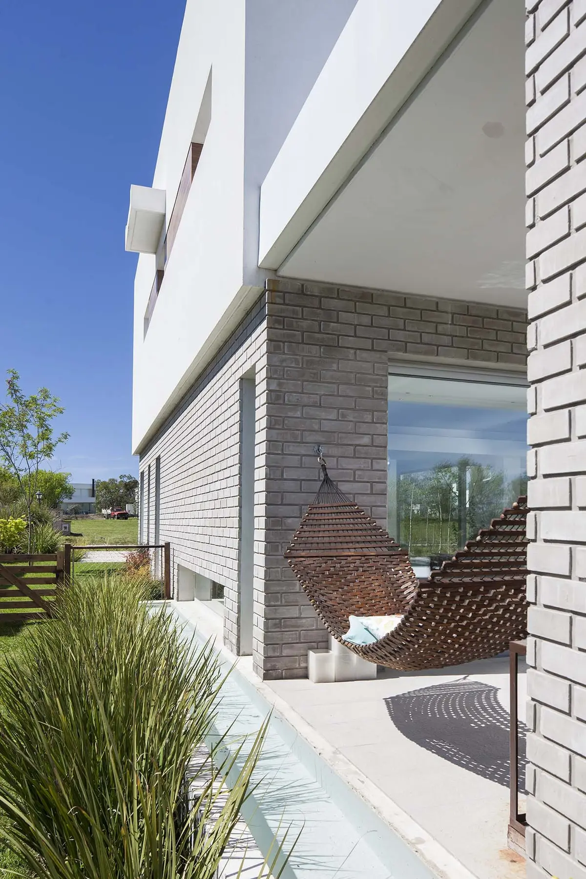 Fachada moderna com detalhes em tijolo e cadeira suspensa — projeto Casa MA, por Estudio GR, em City Bell