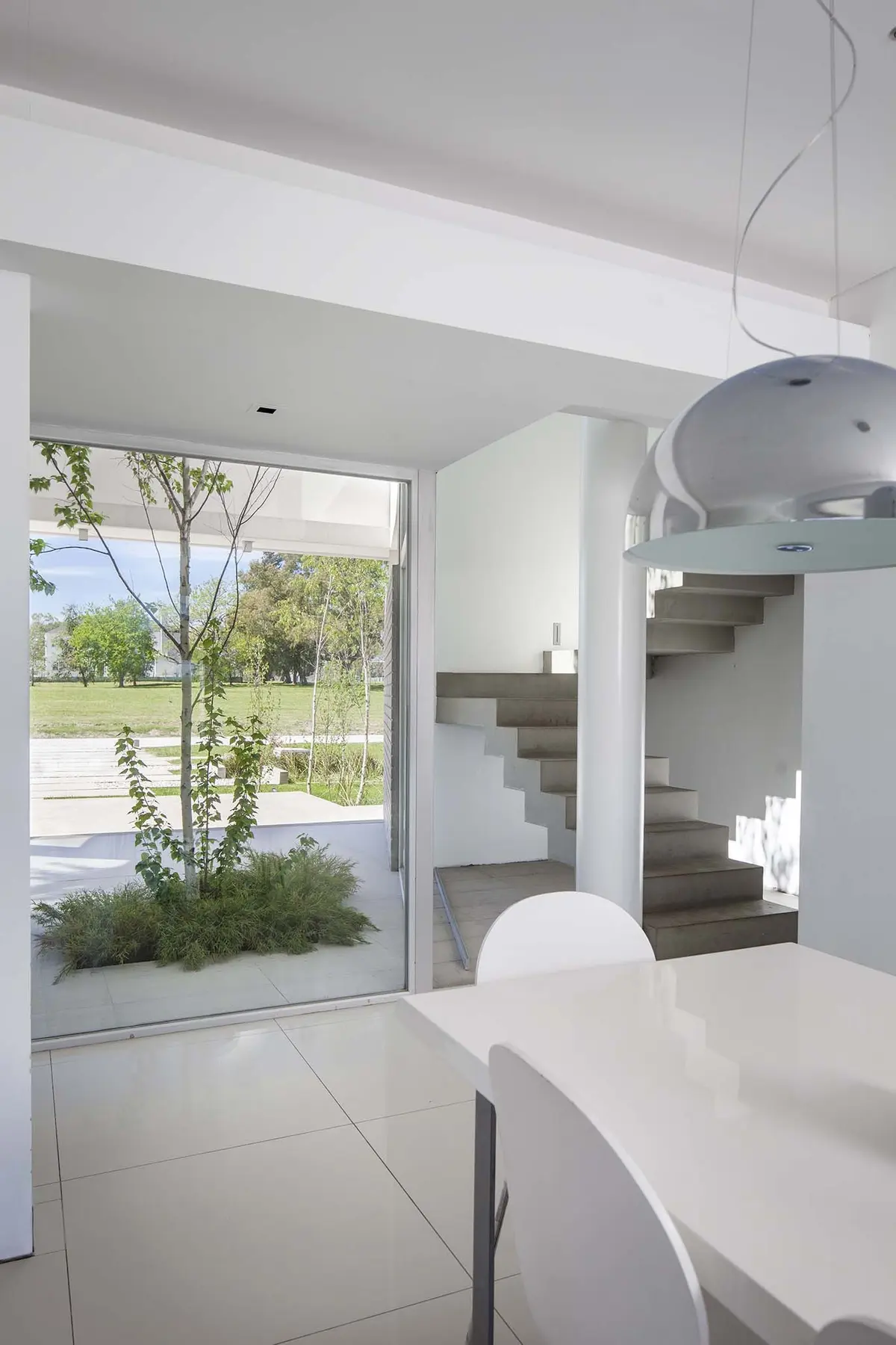 Comedor moderno con vista a patio interior y escalera flotante — proyecto Casa MA, por Estudio GR, en City Bell