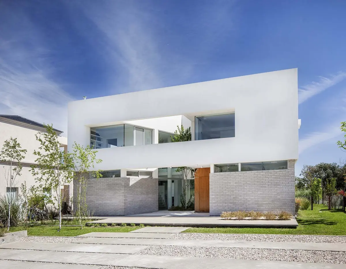 Fachada moderna blanca y de ladrillo con grandes ventanales — proyecto Casa MA, por Estudio GR, en City Bell