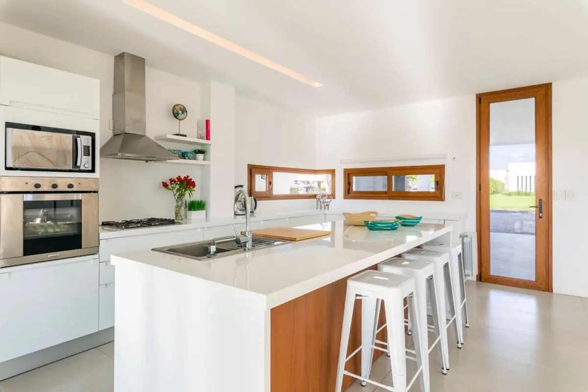 Cocina moderna blanca con isla de cascada y madera — proyecto Casa ME, por Estudio GR, en City Bell