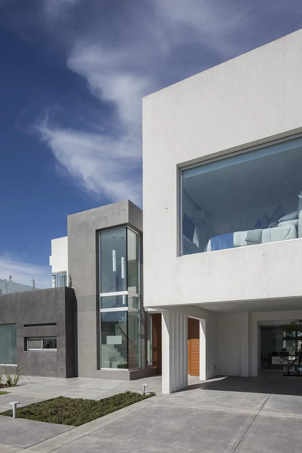 Fachada moderna de hormigón blanco y gris con grandes ventanales y escalera flotante — proyecto Casa FA, por Estudio GR, en City Bell