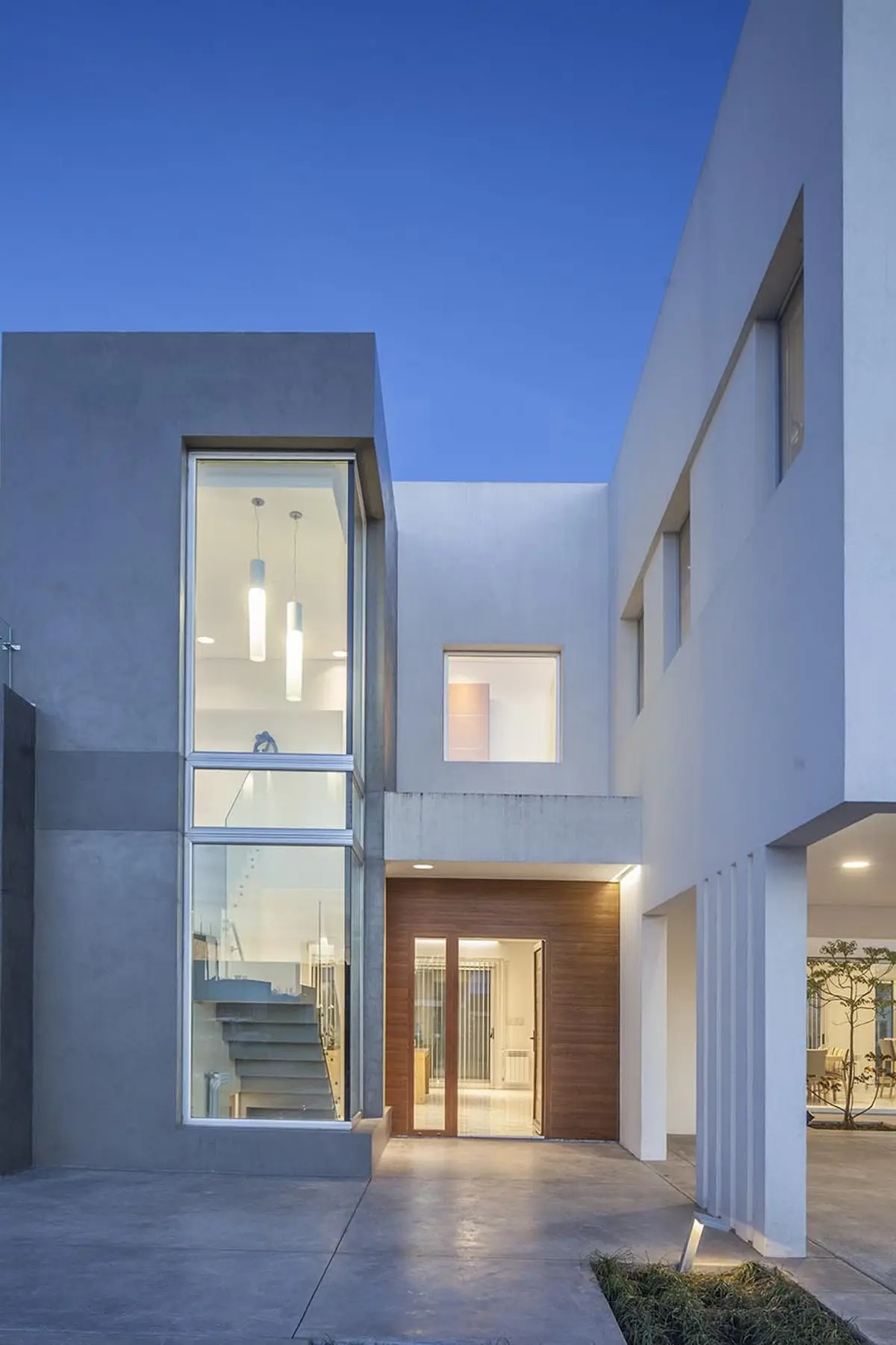 fachada moderna de hormigón con grandes ventanales y entrada de madera — proyecto Casa FA, por Estudio GR, en City Bell