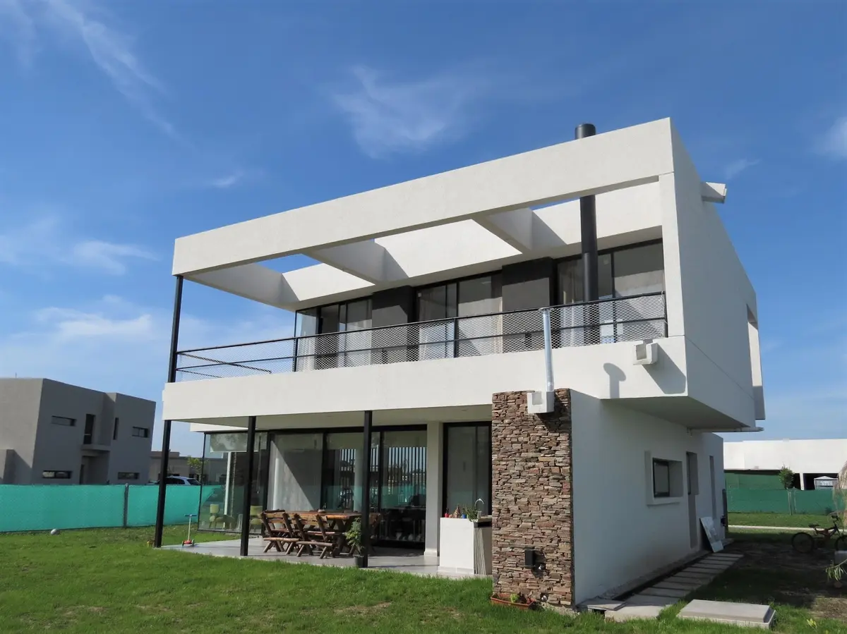 Casa moderna con fachada blanca y detalles de piedra, balcón y jardín — proyecto Casa MB- Harás Sta. María , por Olivieri Arquitectura, en Haras Santa María