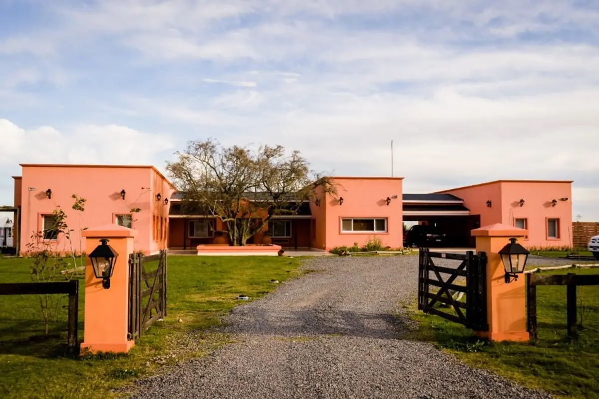 Casa rural rosa com portões e floreiras iluminadas — projeto La casa del árbol, por Estudio Fernandez Long & asoc., em Canning
