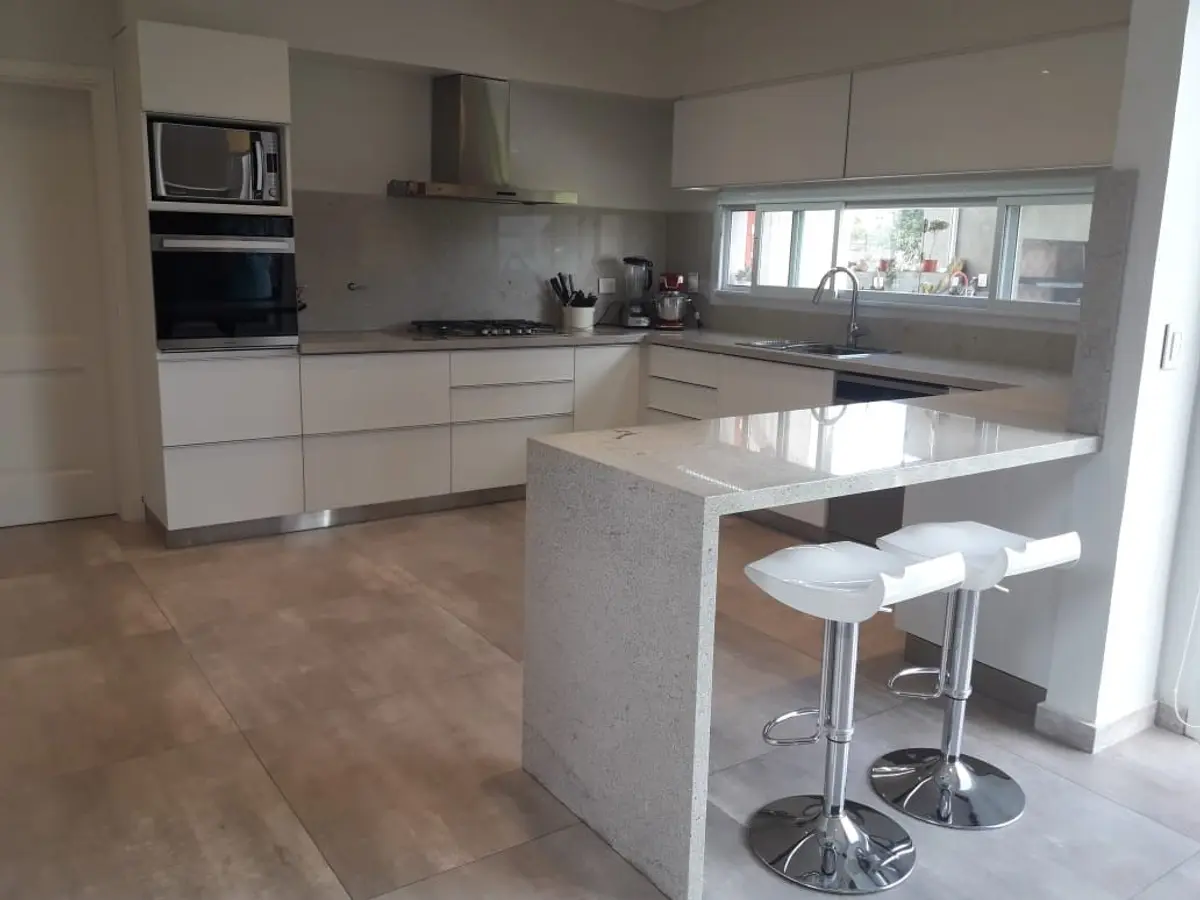 Cozinha moderna com ilha branca, armários brancos e piso bege — projeto Golondrinas 99, por Marcela Romiti Arquitectura, em La Plata