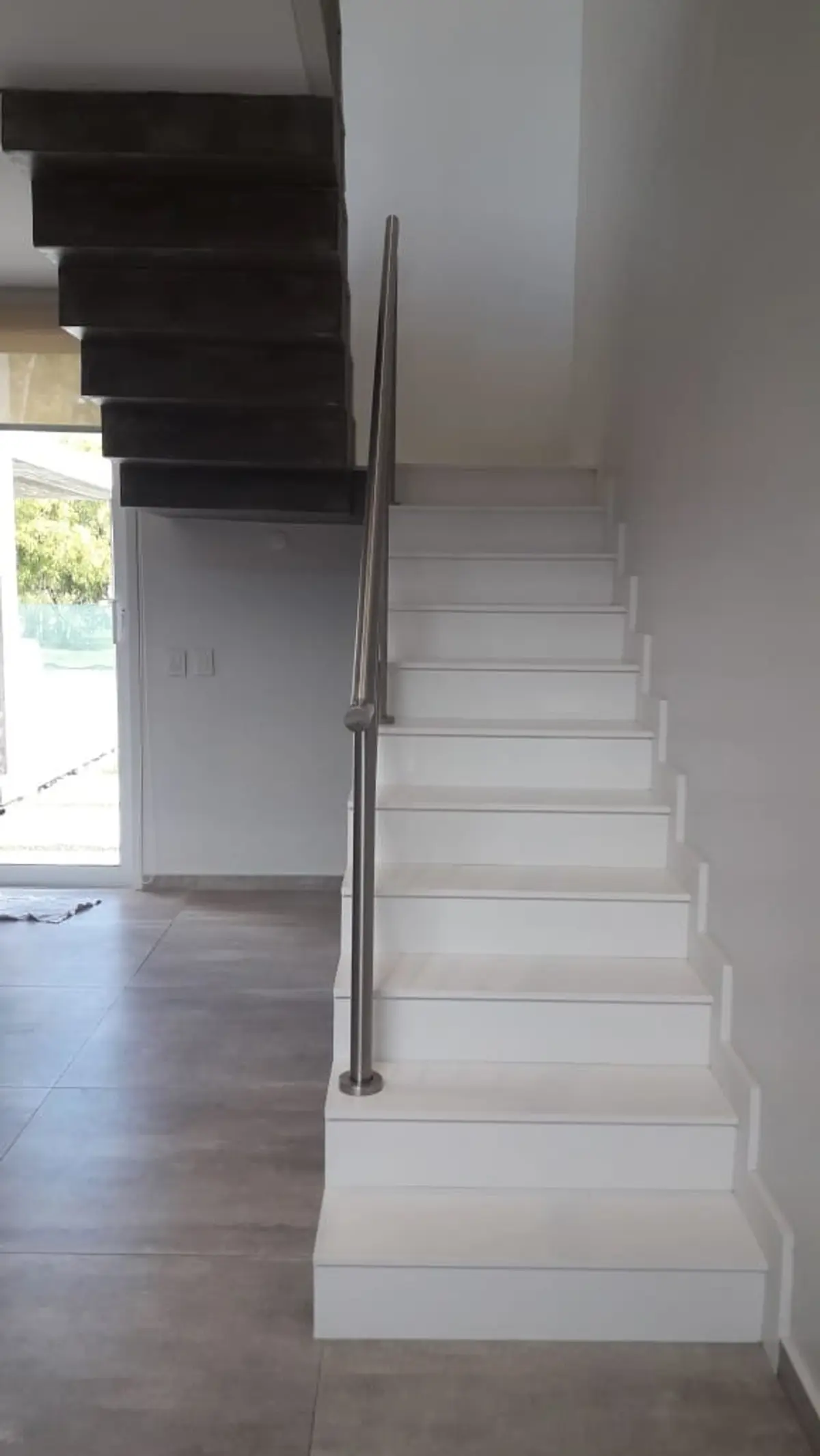 Escada flutuante moderna com corrimão de metal e piso de cerâmica cinza — projeto Golondrinas 99, por Marcela Romiti Arquitectura, em La Plata