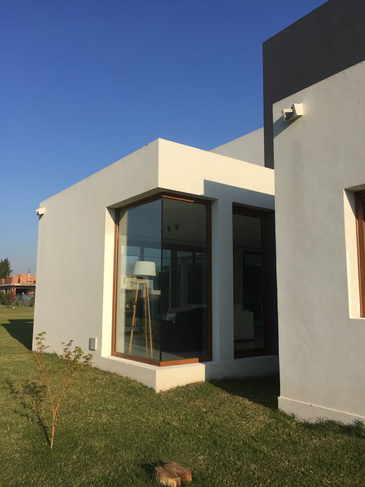 Fachada moderna con ventana de esquina y lámpara de pie visible — proyecto VM, por Estudio GR