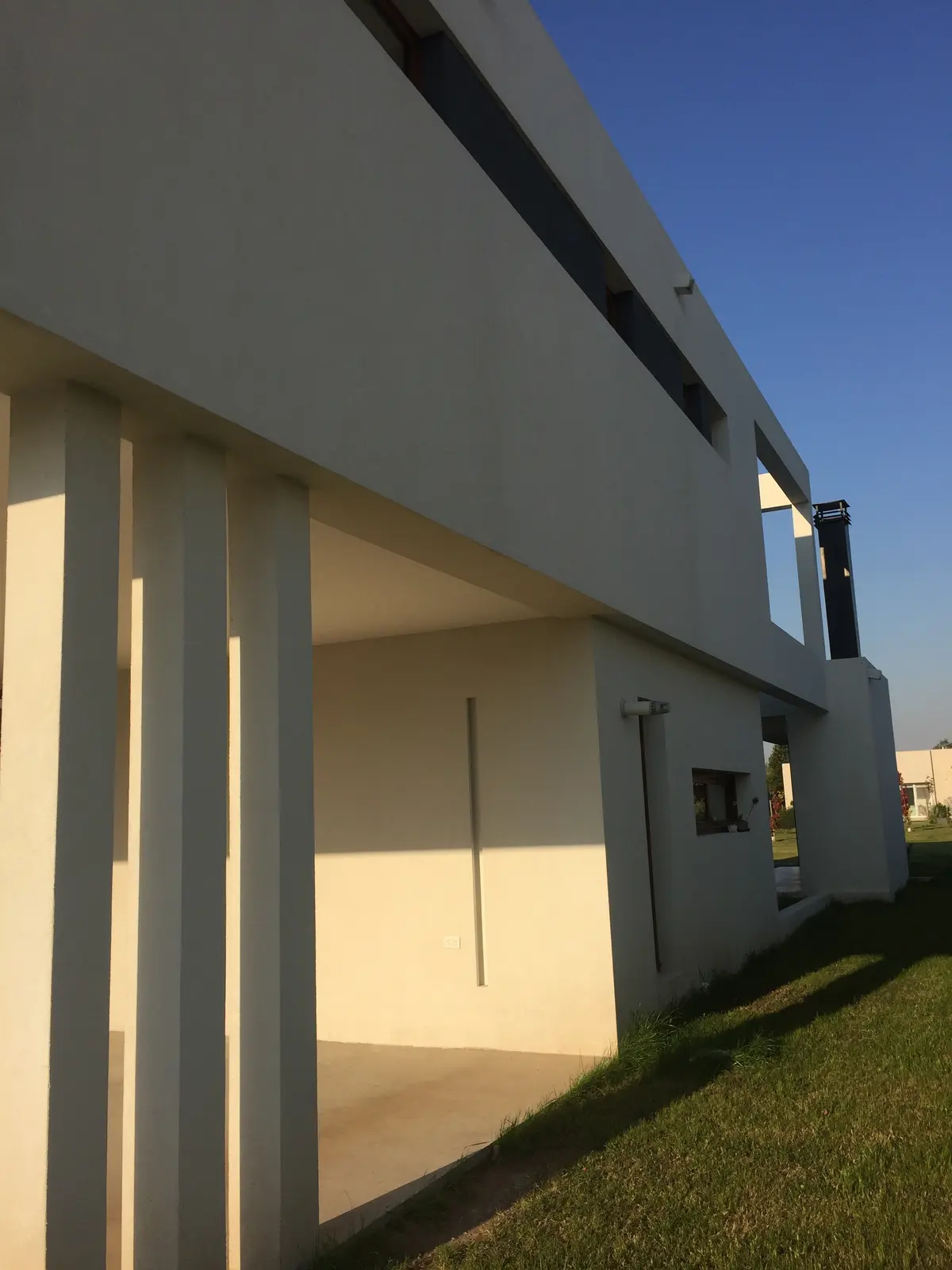 Fachada moderna branca com pilares e sombras, luz natural — projeto VM, por Estudio GR