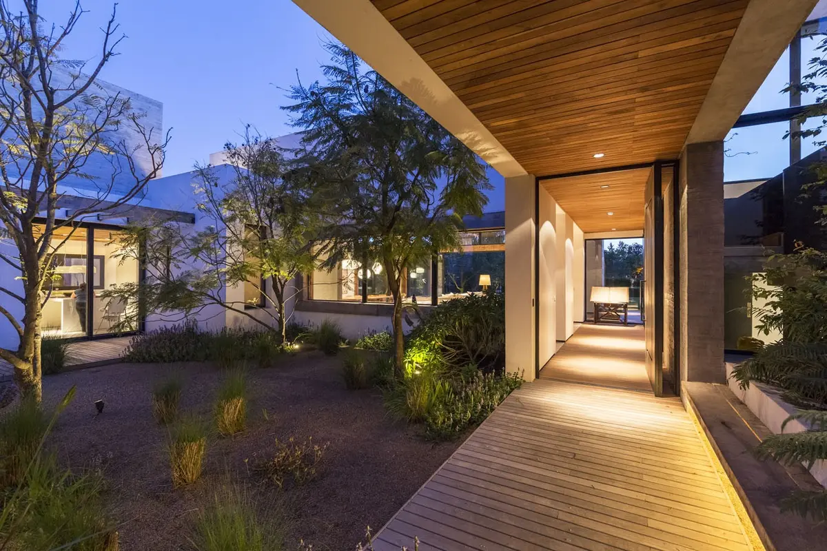 Passarela de madeira iluminada com jardim moderno ao entardecer — projeto Hormigón, Madera y Vidrio, por Ricardo Pereyra Iraola