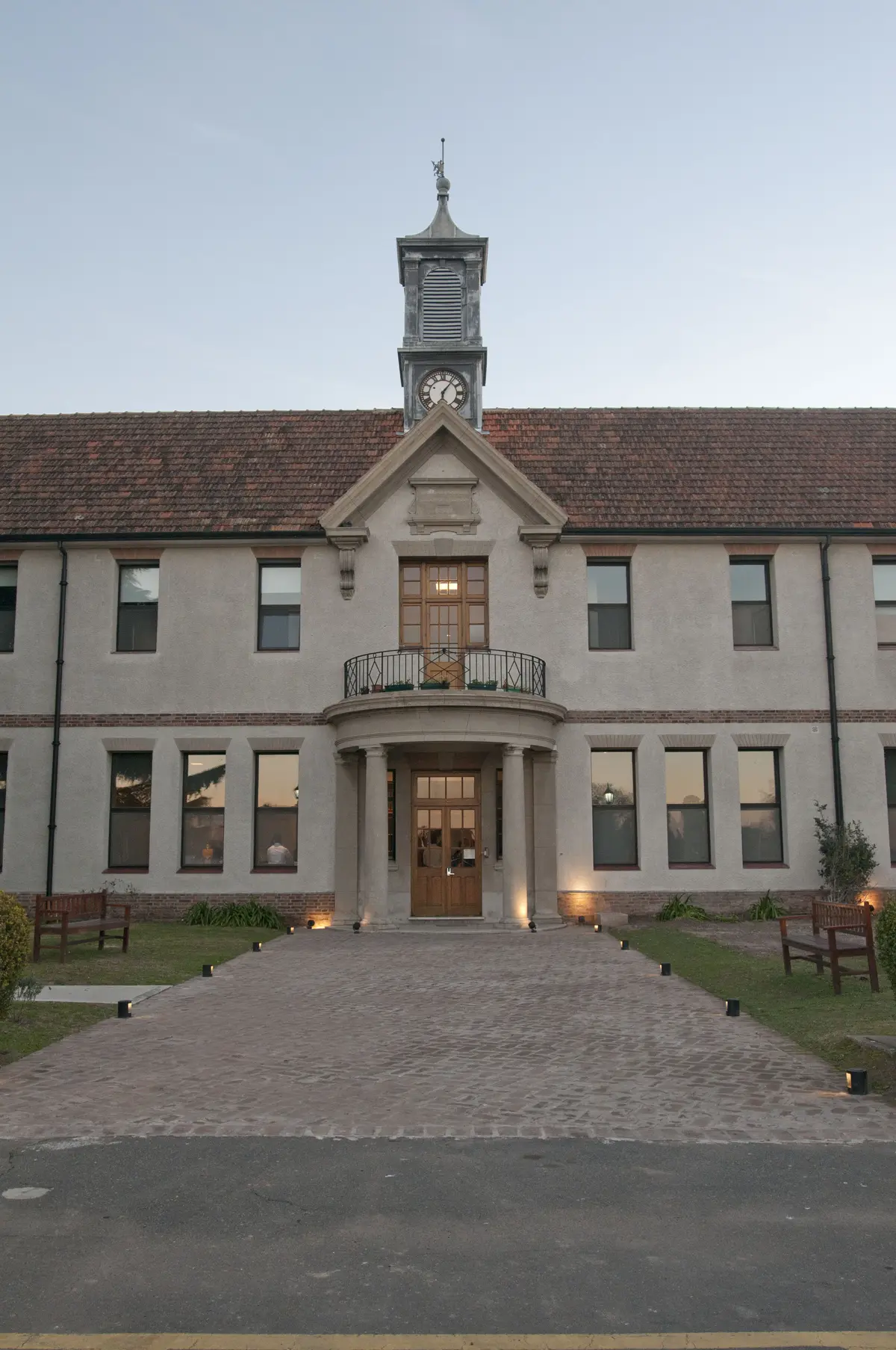 Fachada de edificio clásico con torre de reloj y columnas — proyecto St George´s College Quilmes Edificio Boarding House, por byb.arquitectas, en Quilmes