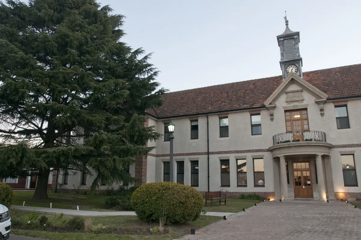 Fachada clásica con torre de reloj y gran árbol — proyecto St George´s College Quilmes Edificio Boarding House, por byb.arquitectas, en Quilmes