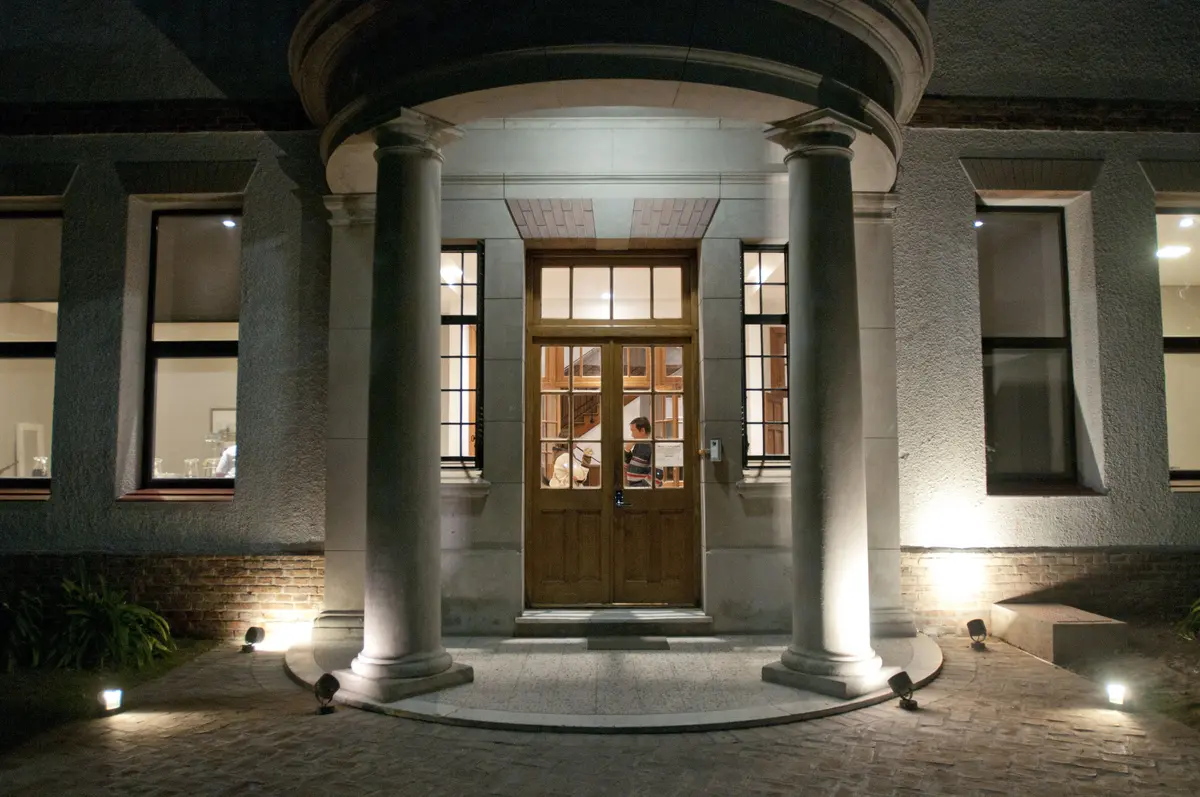 Fachada clássica com colunas de pedra e entrada em arco à noite — projeto St George´s College Quilmes Edificio Boarding House, por byb.arquitectas, em Quilmes