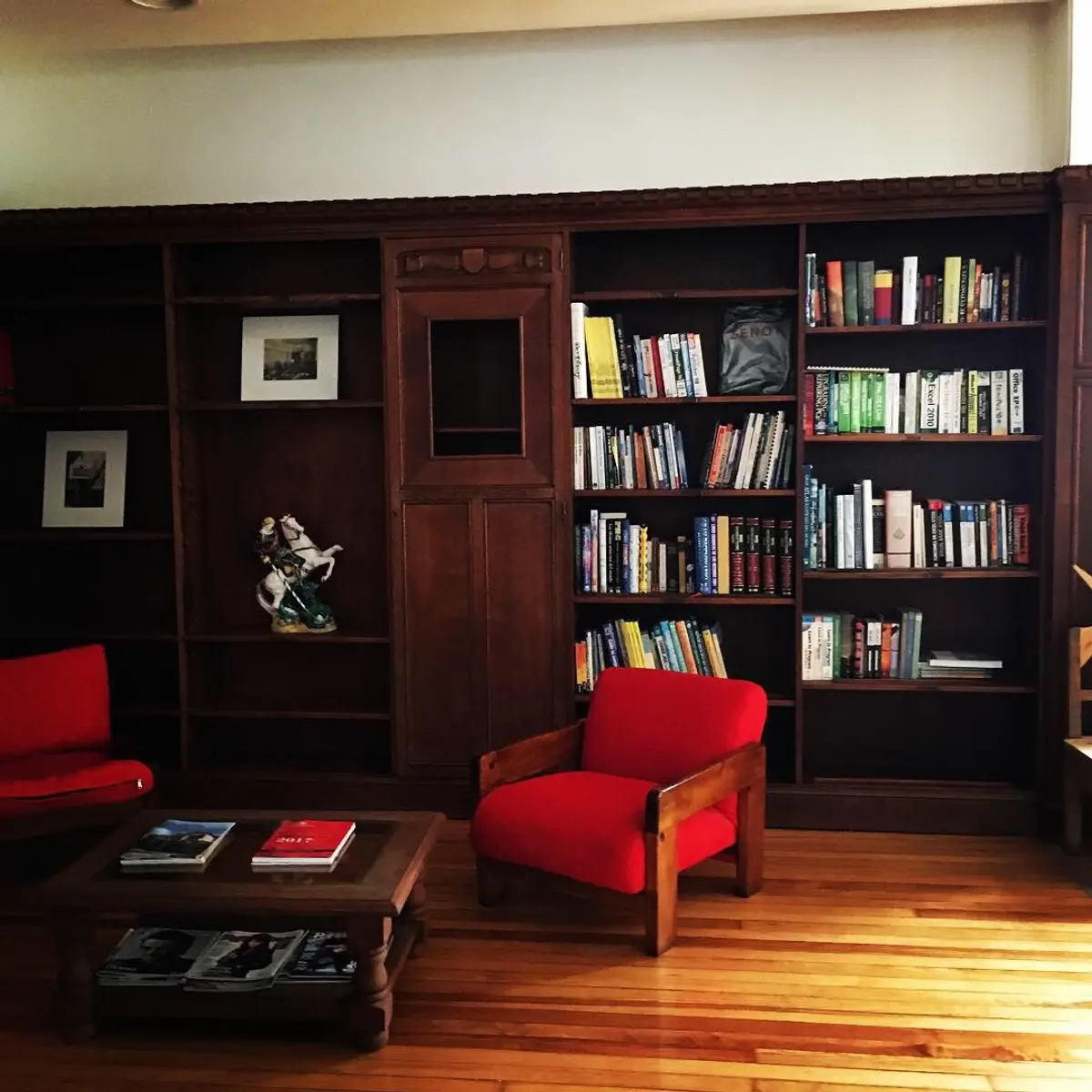 Biblioteca tradicional com poltrona vermelha e estantes cheias — projeto St George´s College Quilmes Edificio Boarding House, por byb.arquitectas, em Quilmes
