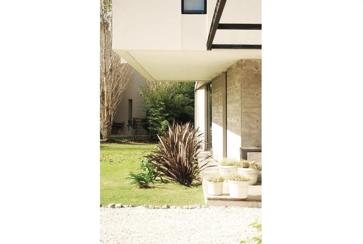 Fachada moderna de concreto branco com amplas janelas e vegetação — projeto casa s, por GARAGE arquitectura, em Rumencó