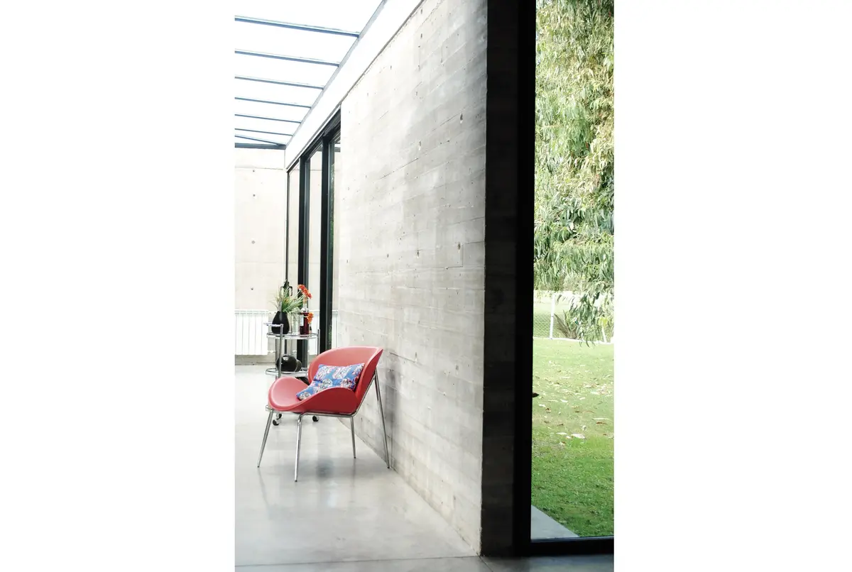 Interior moderno com concreto aparente e destaque para cadeira vermelha — projeto casa s, por GARAGE arquitectura, em Rumencó