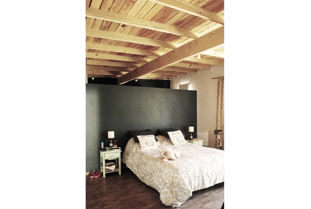 Quarto com vigas de madeira expostas e parede de destaque escura — projeto casa s, por GARAGE arquitectura, em Rumencó