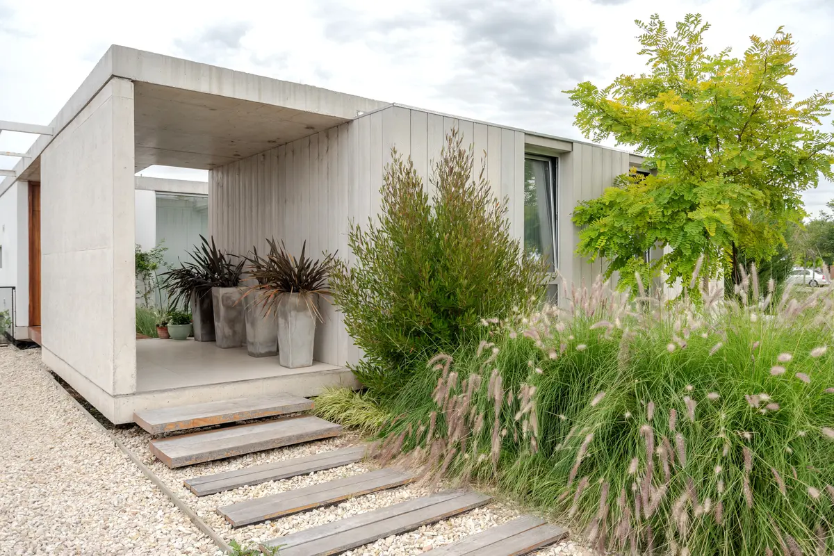 fachada moderna con hormigón, vegetación exuberante y caminos de madera — proyecto casa sr, por GARAGE arquitectura