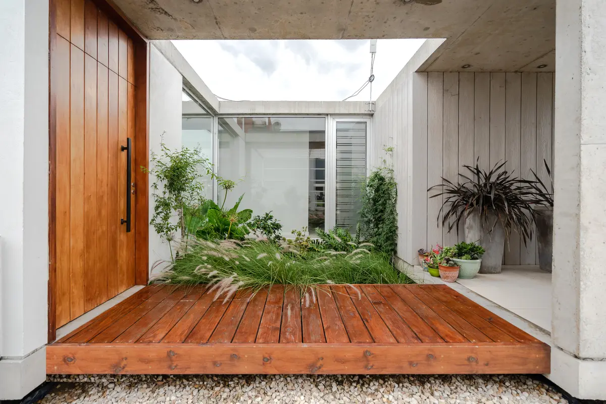 Entrada moderna con deck de madera y vegetación exuberante — proyecto casa sr, por GARAGE arquitectura